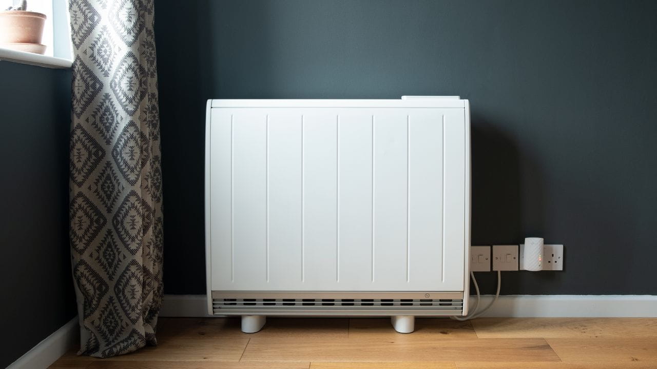 Weisse Elektroheizung an einer dunklen Wand neben einem Fenster in einem Innenraum.