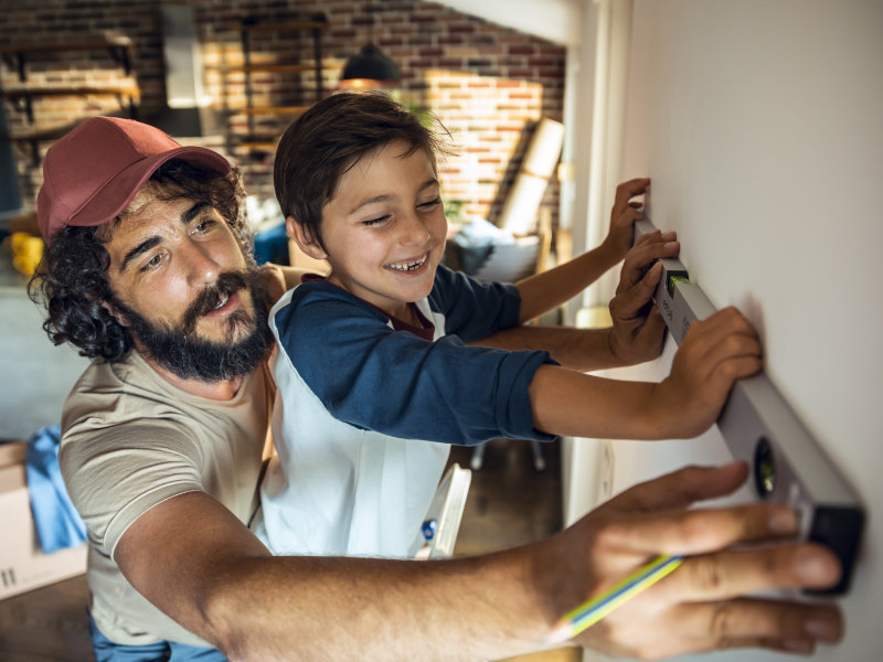 Vater und Kind messen gemeinsam eine Wand mit einer Wasserwaage