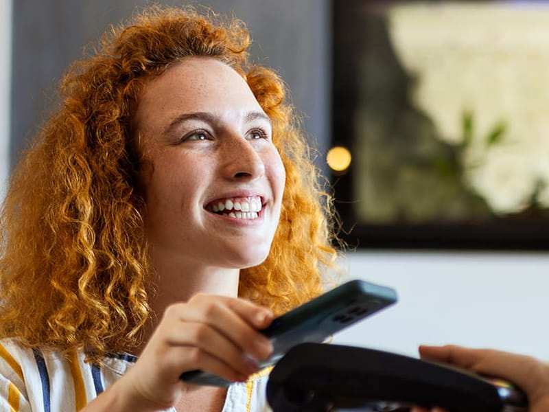 Frau bezahlt im Restaurant mit dem Smartphone an einem mobilen Zahlungsterminal.