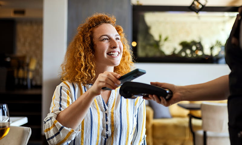 Frau bezahlt im Restaurant mit dem Smartphone an einem mobilen Zahlungsterminal.