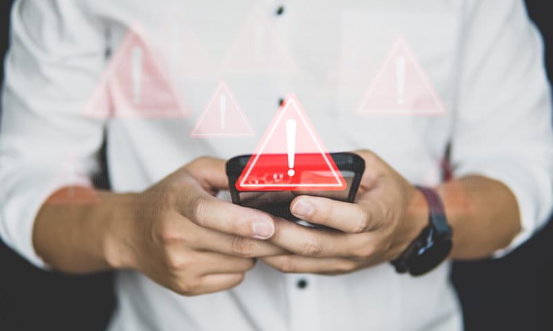 Person hält ein Smartphone, darüber erscheinen Warnsymbole mit Ausrufezeichen