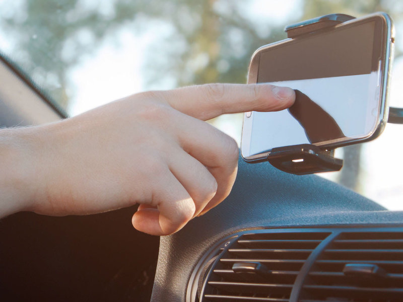 Hand bedient ein Smartphone in einer Halterung im Auto für Navigation oder Standortsuche