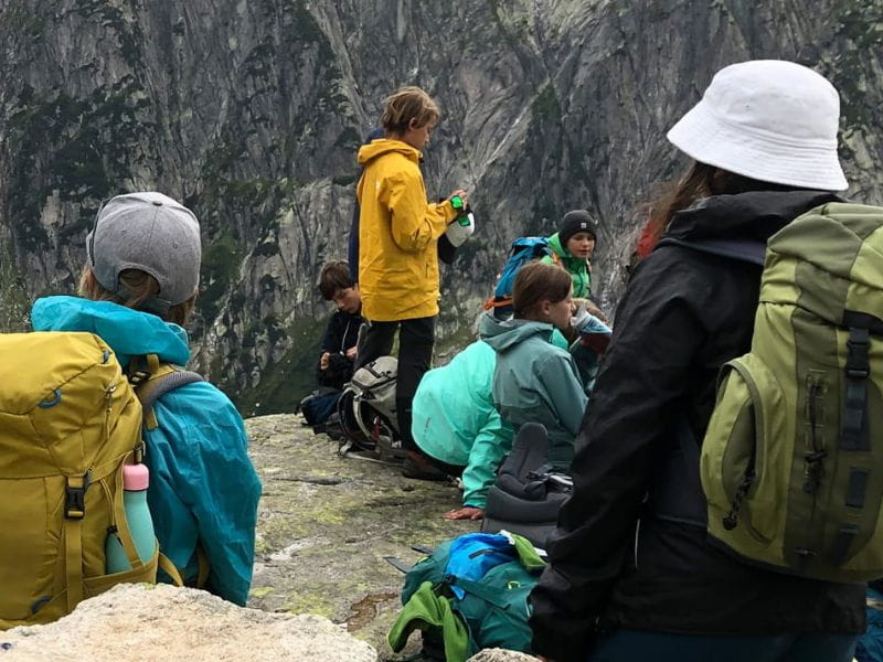 Schülerinnen und Schüler mit Rucksäcken machen während eines Klassenlagers Rast in den Bergen.