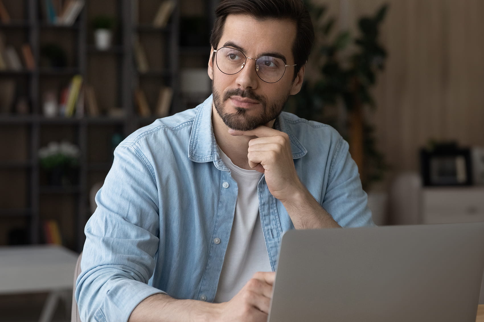 Mann sitzt am Tisch, blickt auf einen Laptop und stützt das Kinn auf die Hand