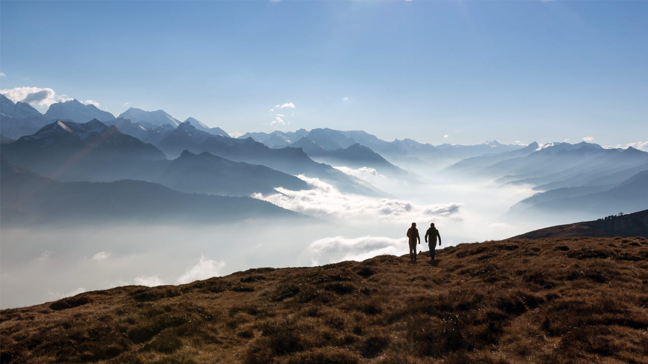 Zwei Menschen wandern auf einem Berggrat mit Blick über ein Nebelmeer und die Alpen
