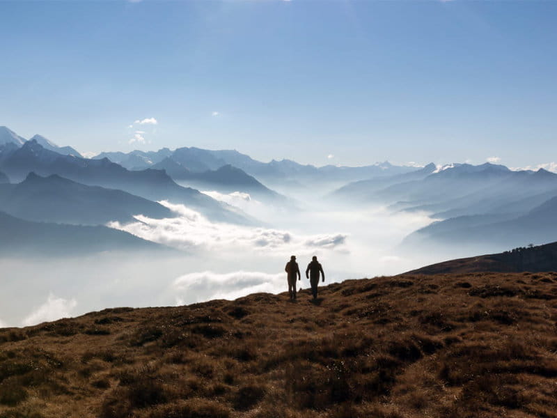 Zwei Menschen wandern auf einem Berggrat mit Blick über ein Nebelmeer und die Alpen