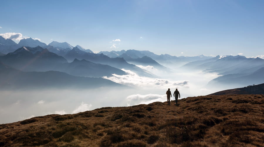 Zwei Menschen wandern auf einem Berggrat mit Blick über ein Nebelmeer und die Alpen