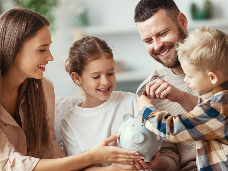 Familie sitzt zusammen und legt Geld in ein Sparschwein