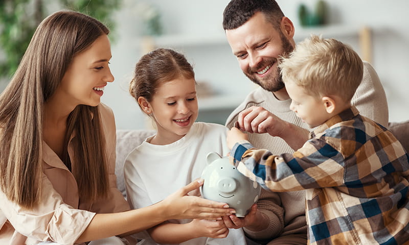 Familie sitzt zusammen und legt Geld in ein Sparschwein