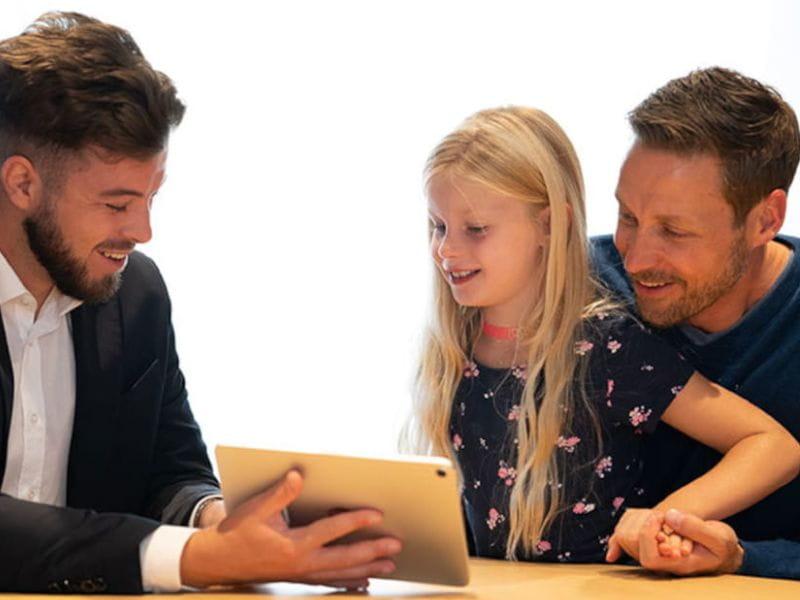 Ein Berater zeigt Vater und dessen Tochter etwas auf einem Tablet.