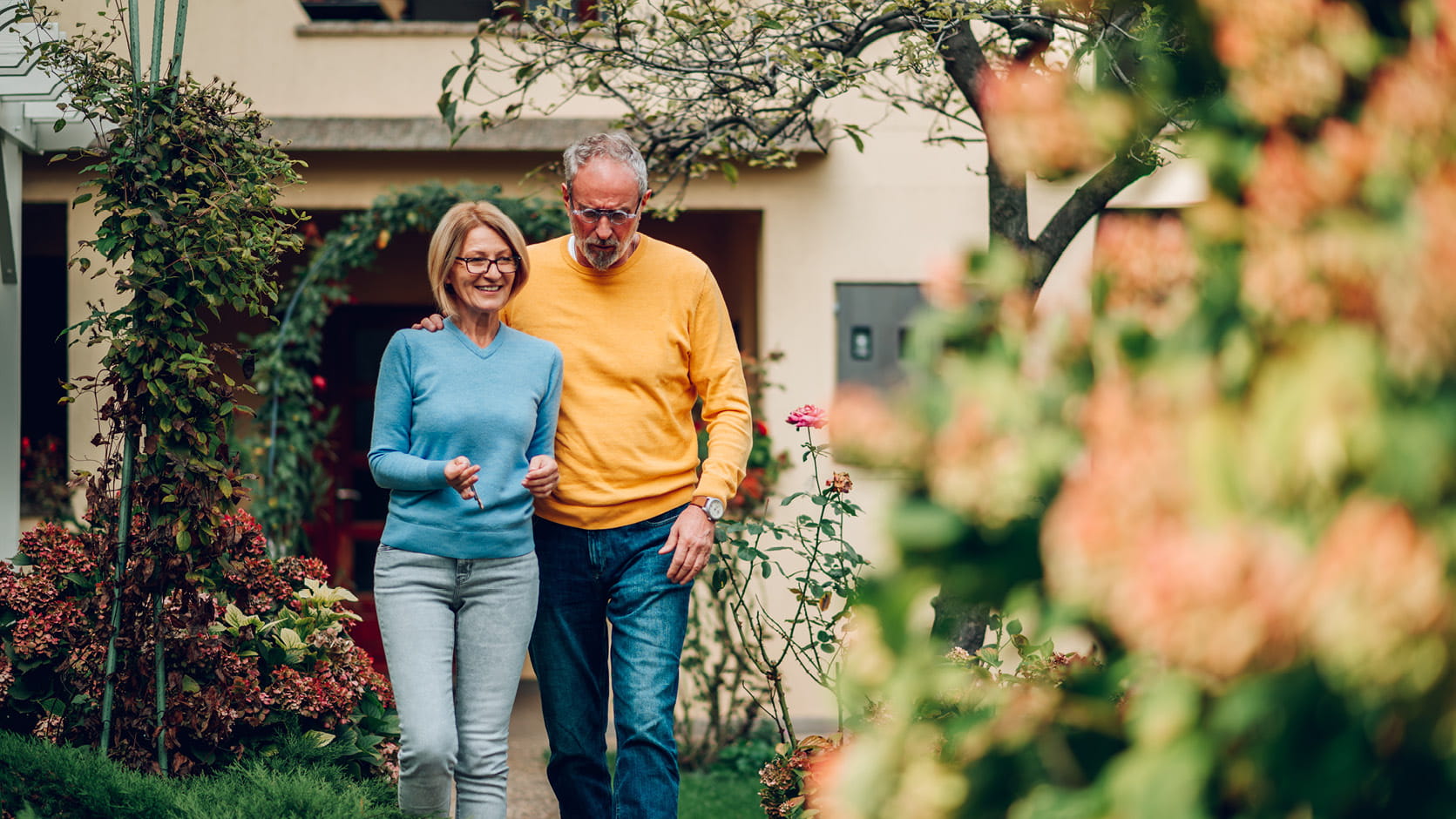 Älteres Paar geht gemeinsam durch einen Garten vor dem Haus