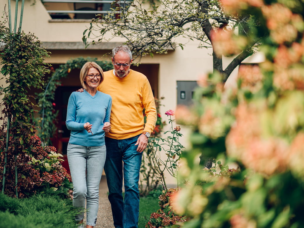 Älteres Paar geht gemeinsam durch einen Garten vor dem Haus